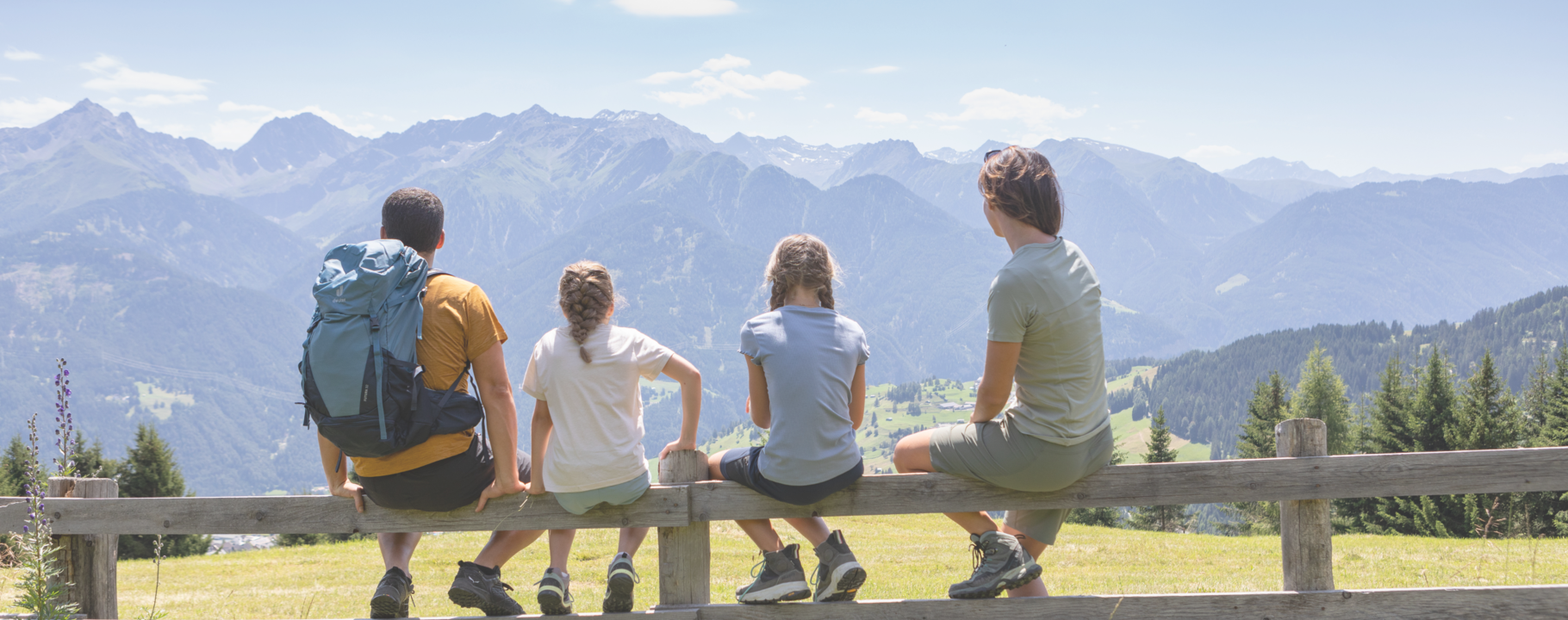 Two children and their parents sit on a fence, gazing at a valley landscape | © Serfaus-Fiss-Ladis Marketing GmbH | Andreas Kirschner